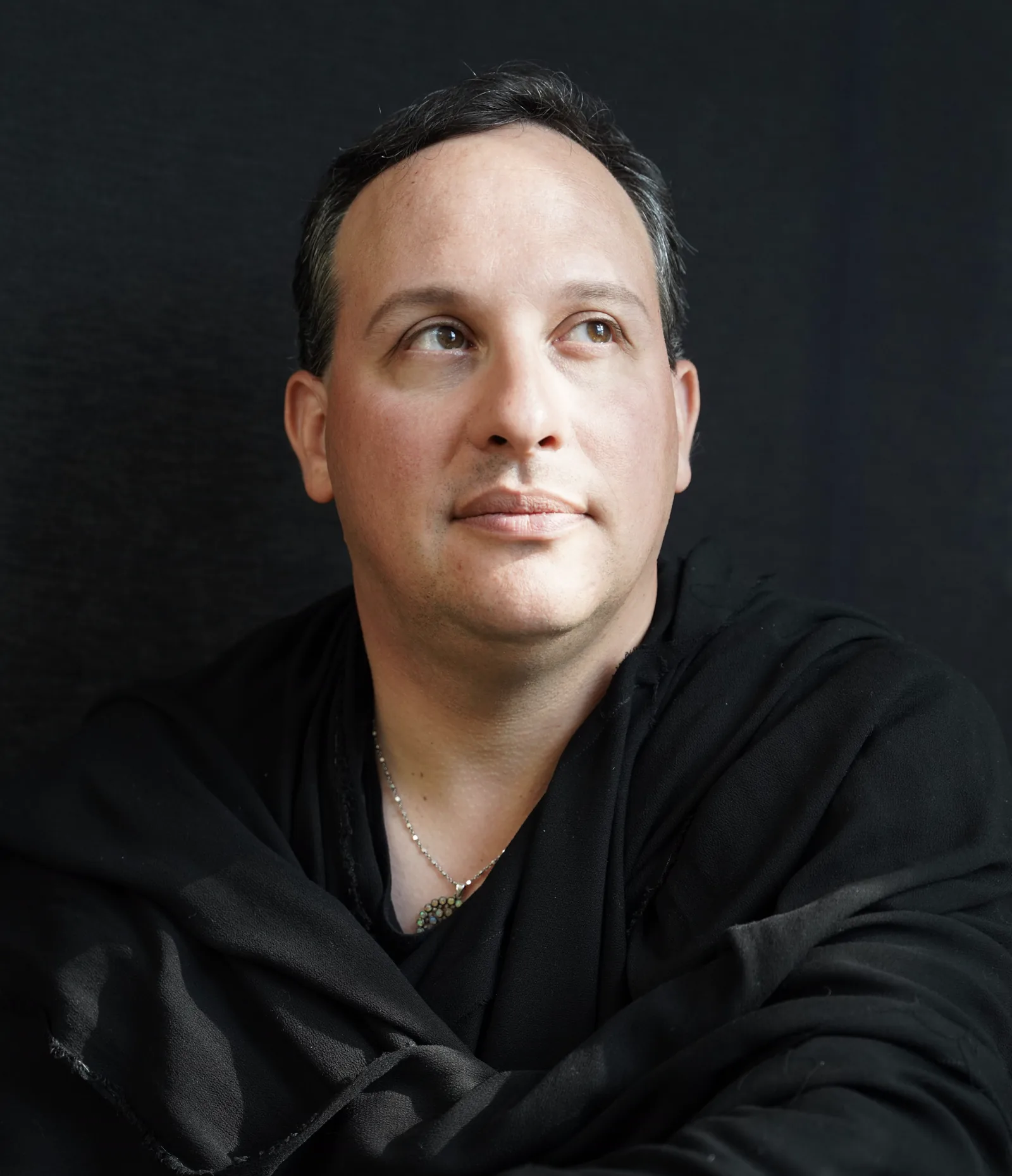Brian Baruch looking upward, wearing a black wrap and a pendant
